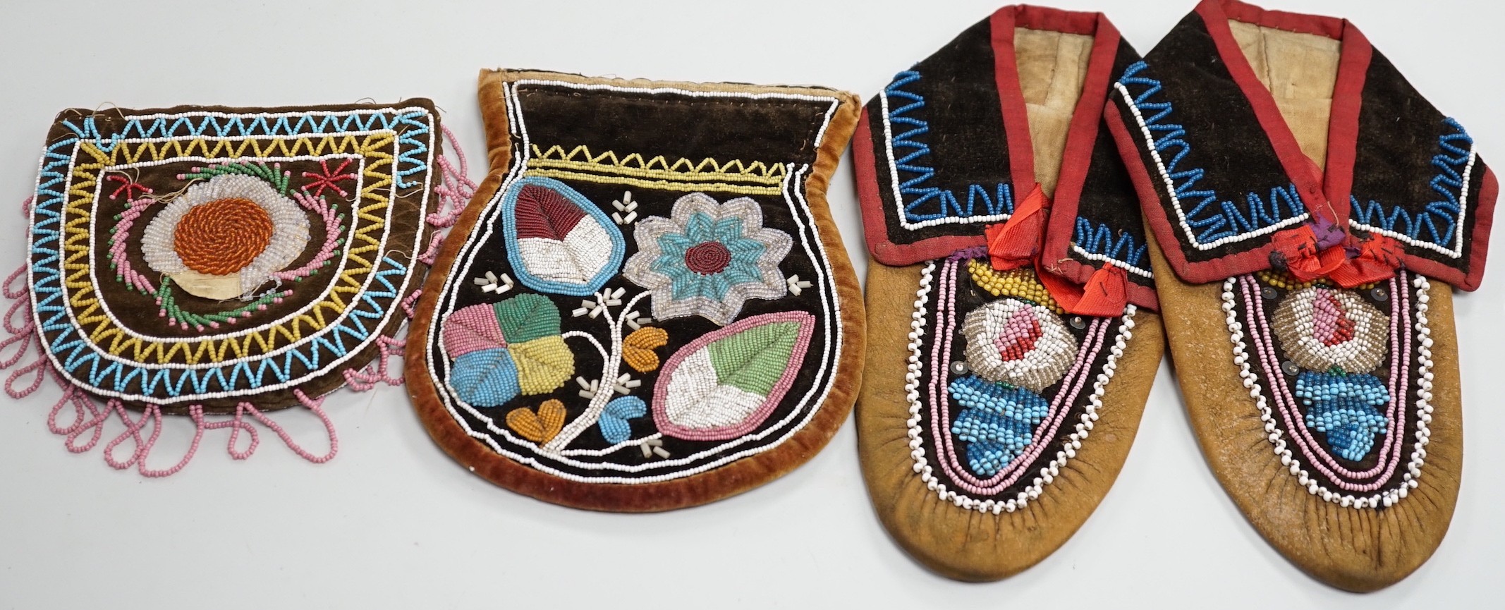 A pair of mid to late 19th century Mikmaq, North American Indian, moccasins, worked in floral beadwork on vamp, with velvet cuffs and red silk ties, together with two Wabanaki floral bead-worked velvet bags